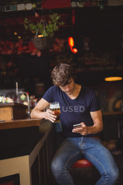 Чоловік використовує мобільний телефон, маючи келих пива в барі — стокове фото