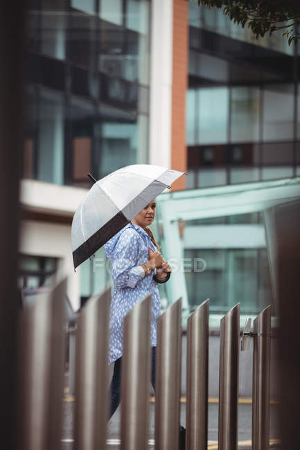 Enfoque selectivo de hermosa mujer sosteniendo paraguas y caminando en la calle durante la temporada de lluvias - foto de stock