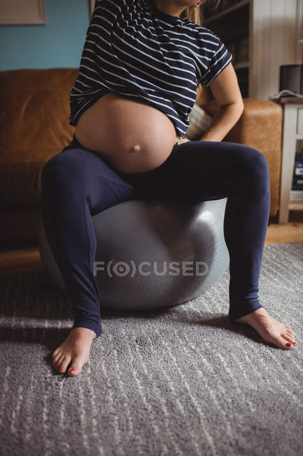 Image recadrée de femme enceinte effectuant des exercices d'étirement sur balle de fitness dans le salon — Photo de stock