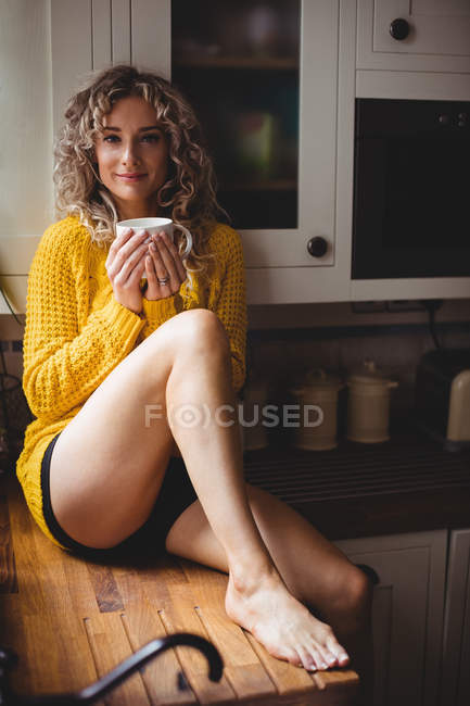 Retrato de una hermosa mujer tomando café en la cocina en casa - foto de stock