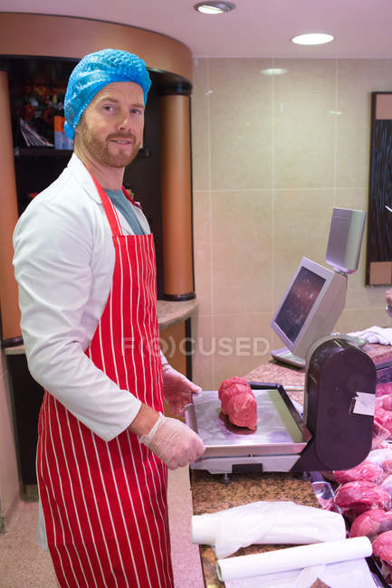 Retrato de açougueiro verificando o peso da carne no balcão em loja de carne — Fotografia de Stock