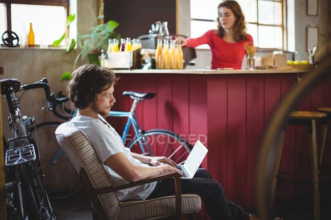 Uomo seduto sulla sedia e utilizzando il computer portatile in negozio di biciclette — Foto stock