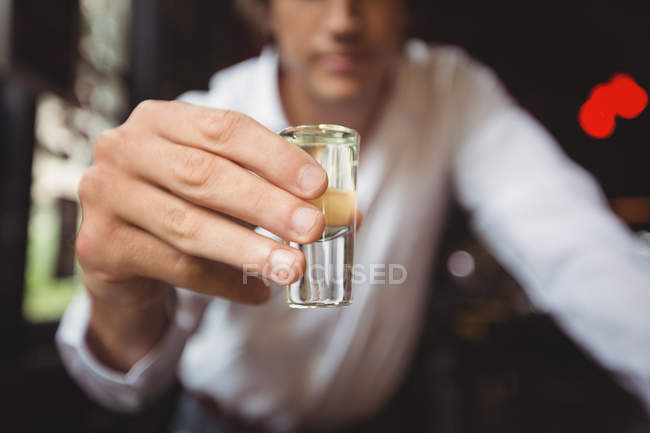Primer plano del camarero sosteniendo el vaso de tequila en el mostrador de la barra en el bar - foto de stock