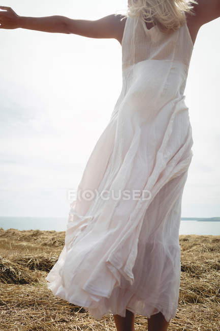 Rear view of carefree blonde woman in white dress standing on field at sunny day — Stock Photo