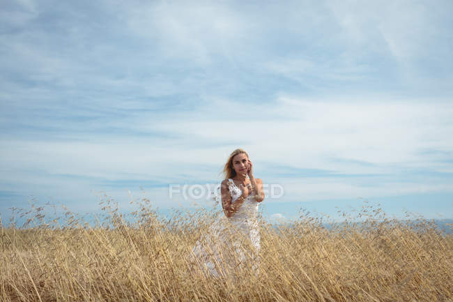 Despreocupada mujer rubia de pie en el campo y mirando a la cámara - foto de stock