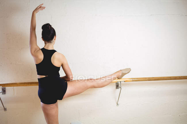 Visão traseira da bailarina alongando-se no barre enquanto pratica dança de balé no estúdio — Fotografia de Stock