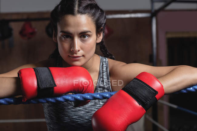 Portrait of Tired boxer in boxing gloves leaning on ropes of boxing ring at fitness studio — Stock Photo