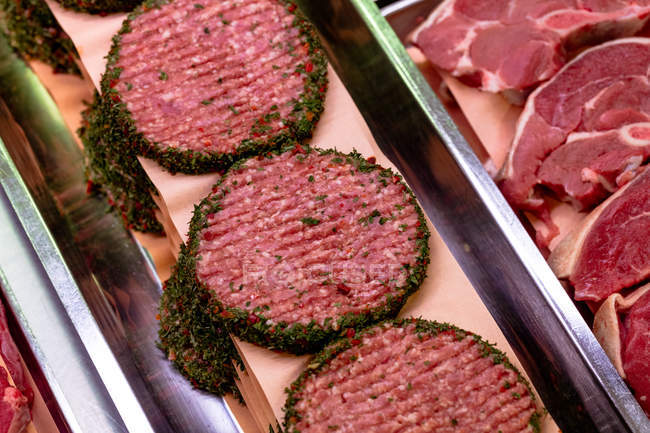 Galettes de viande marinées au comptoir d'exposition dans la boucherie — Photo de stock
