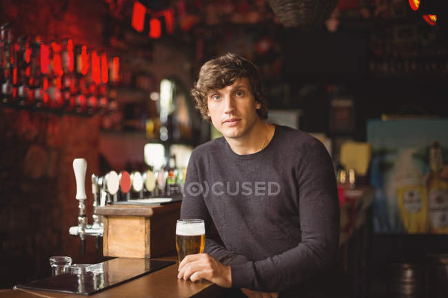 Retrato del hombre con un vaso de cerveza en el mostrador del bar en el bar - foto de stock