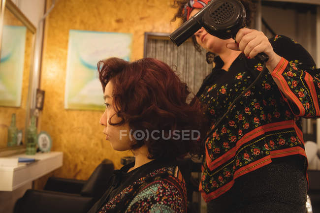 Peluquero secador de pelo pelo del cliente en un salón profesional - foto de stock