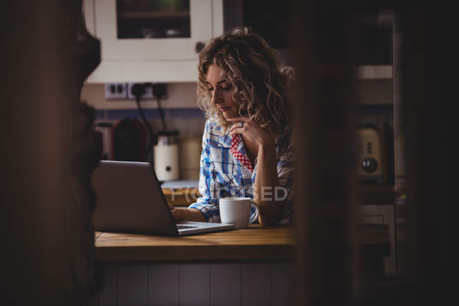 Женщина использовала ноутбук, когда пила кофе на кухне дома — стоковое фото