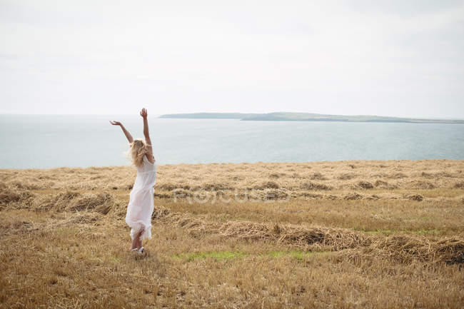 Rückansicht einer blonden Frau, die mit offenen Armen auf einem Feld steht — Stockfoto