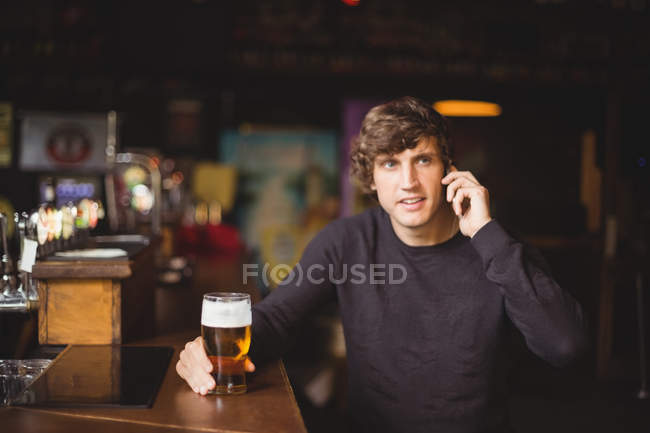 Hombre hablando por teléfono móvil en bar con vaso de cerveza en la mano - foto de stock