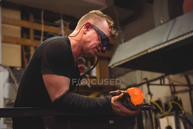 Glassblower shaping molten glass piece with wet cloth at glassblowing factory — Stock Photo