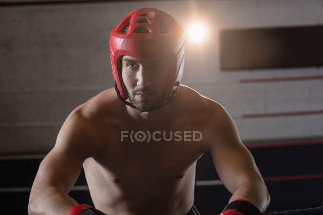 Male boxer in protective boxing helmet leaning on ropes of boxing ring at fitness studio — Stock Photo