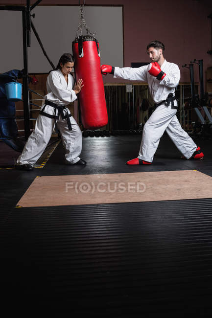 Uomo e donna che praticano karate con sacco da boxe in studio — Foto stock