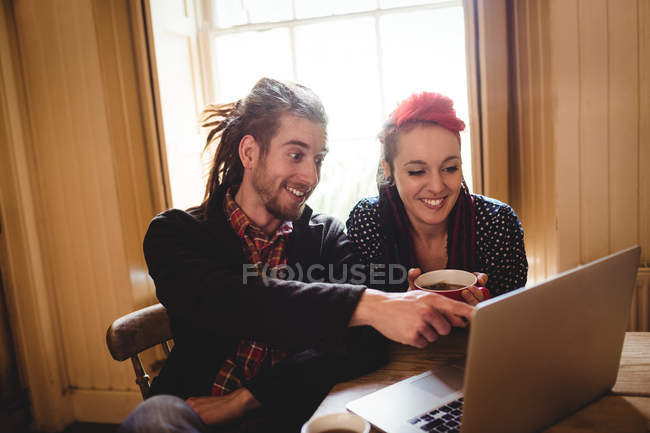 Casal sorrindo usando laptop enquanto sentado à mesa — Fotografia de Stock
