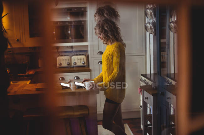 Красива жінка використовує цифровий планшет, маючи каву на кухні вдома — стокове фото