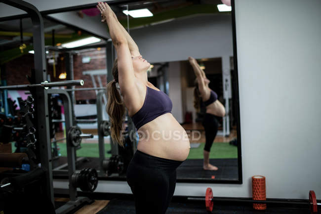 Беременная женщина выполняет упражнения на растяжку в тренажерном зале — стоковое фото
