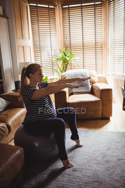 Side view of Pregnant woman performing stretching exercise on fitness ball in living room at home — Stock Photo