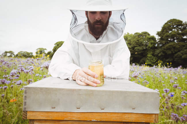 Бджоляр тримає пляшку меду на вулику в полі — стокове фото