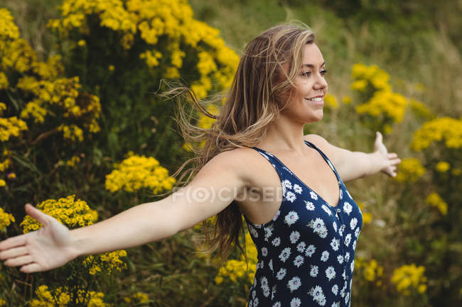 Femme debout avec les bras tendus dans la prairie par une journée ensoleillée — Photo de stock
