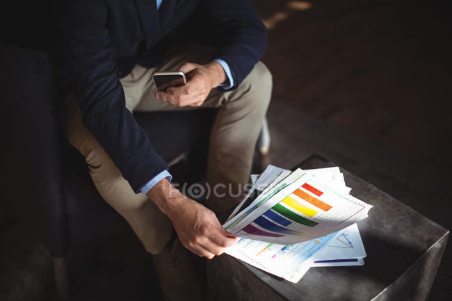 Businessman with mobile phone checking financial reports in the office — Stock Photo
