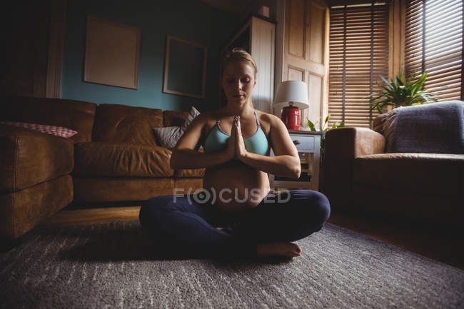 Attractive Pregnant woman performing yoga in living room at home — Stock Photo