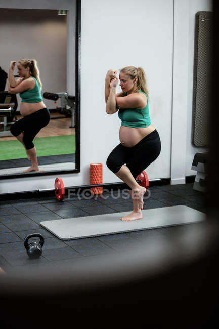 Вагітна жінка виконує вправи на тренувальному килимку в тренажерному залі — стокове фото