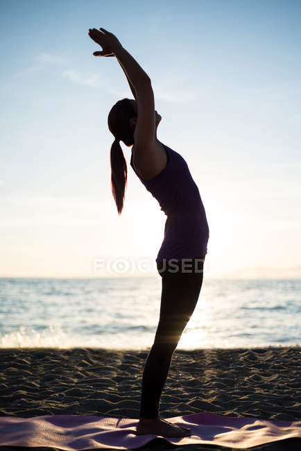 Vista lateral da mulher realizando ioga na praia no dia ensolarado — Fotografia de Stock