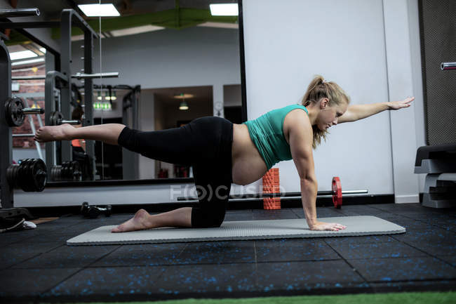 Вагітна жінка, виконуючи розтяжку вправи на тренувальному килимку в тренажерному залі — стокове фото
