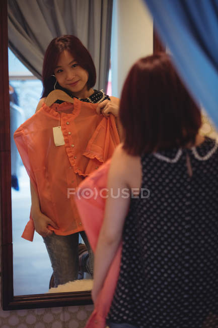 Mujer mirando el espejo mientras intenta una parte superior en la tienda boutique - foto de stock