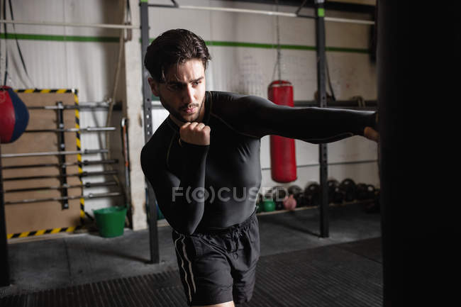 Retrato de boxeador masculino practicando boxeo con saco de boxeo en gimnasio - foto de stock