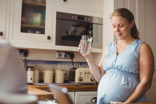 Pregnant woman drinking water in kitchen at home — Stock Photo