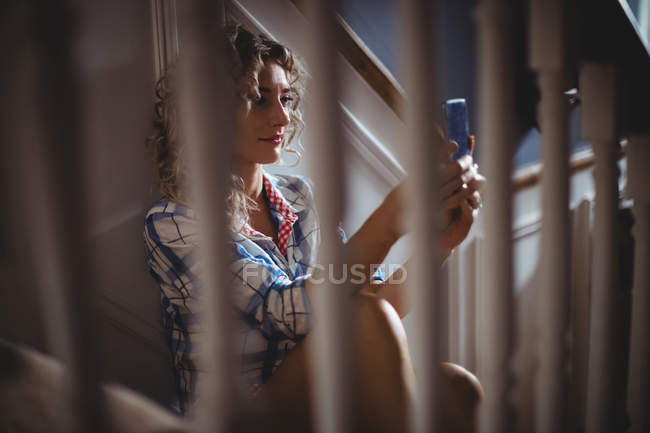 Красива жінка сидить на сходах, використовуючи мобільний телефон вдома — стокове фото
