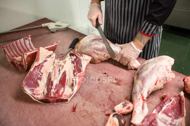 Mid section of butcher cutting the ribs of pork carcass in butchers shop — Stock Photo