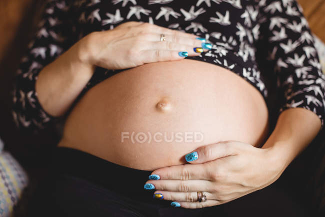 Обрізане зображення вагітної жінки, що розслабляє і зворушує живіт у вітальні — стокове фото