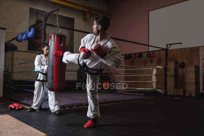 Esportista e esportista praticando karatê com saco de perfuração em estúdio — Fotografia de Stock