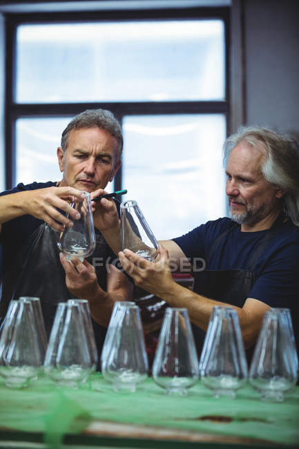 Soplador de vidrio y un colega examinando cristalería en la fábrica de soplado de vidrio - foto de stock