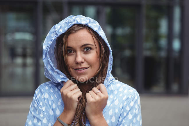 Красива жінка у вітряній вітрильниці дивиться на камеру під час дощу — стокове фото