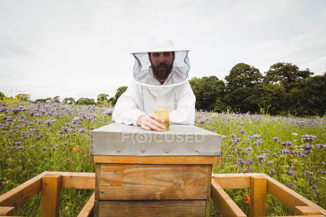 Пчеловод держит бутылку меда на пчелином улее в поле — стоковое фото