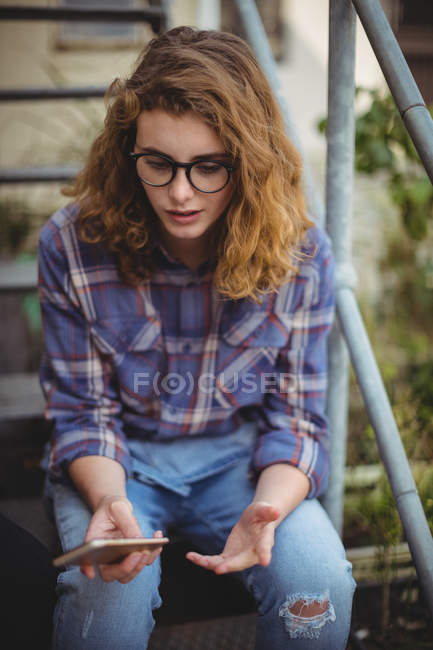Woman sitting on stairs and using mobile phone outside house — Stock Photo