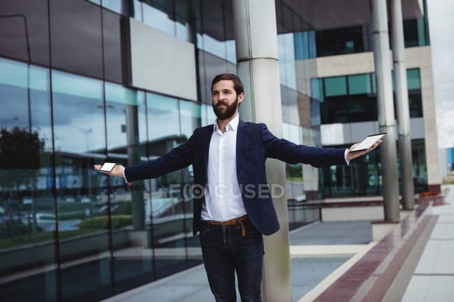 Businessman holding mobile phone and digital tablet in office premises — Stock Photo