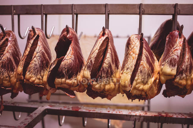 Corazones de ternera colgando en una fila en el almacén en la carnicería - foto de stock