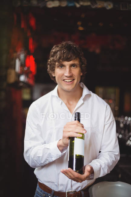 Portrait of bar tender holding a bottle of wine at bar — Stock Photo