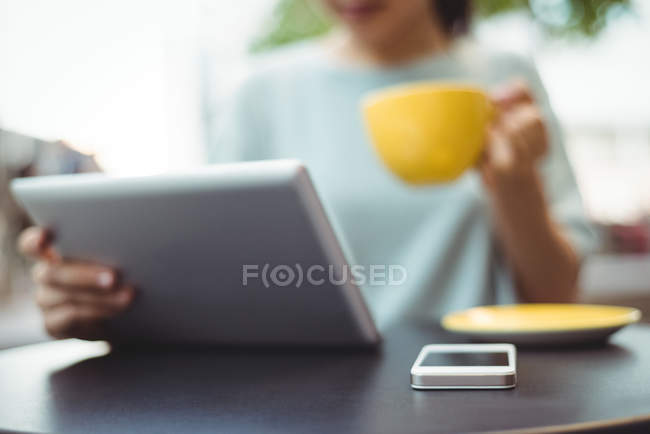 Woman using digital tablet while having coffee in cafe — Stock Photo