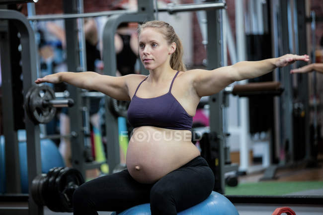 Donna incinta che preforma esercizio di stretching sulla palla fitness in palestra — Foto stock