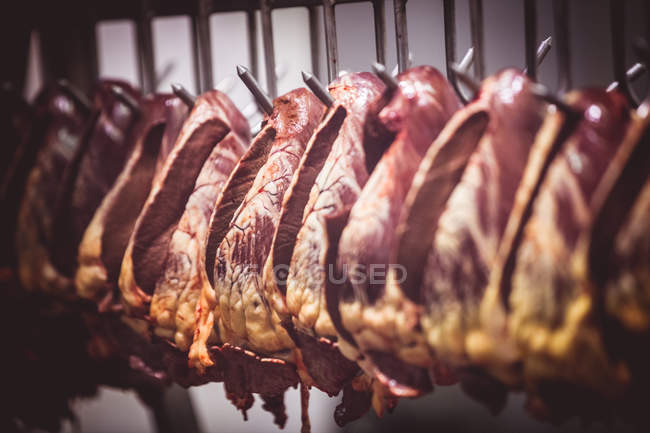 Close-up de corações de carne de vaca pendurados em uma fileira na sala de armazenamento no açougue — Fotografia de Stock