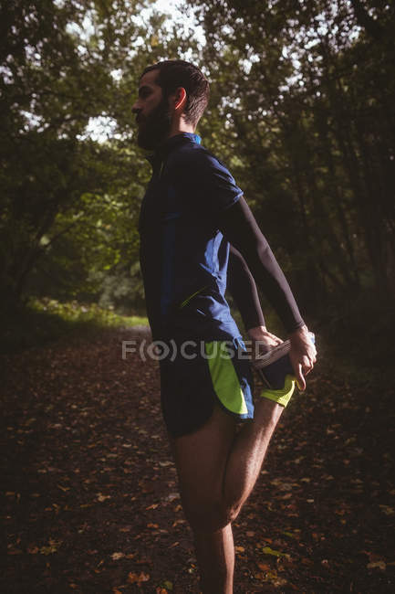 Atleta realizando ejercicio de estiramiento en el bosque - foto de stock