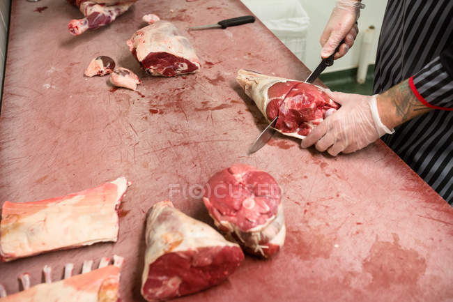 Sección media del carnicero cortando la canal de cerdo con un cuchillo en la carnicería - foto de stock